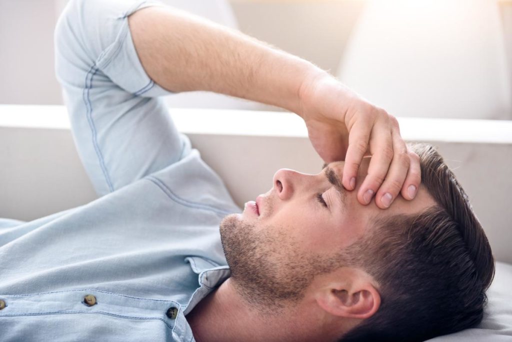 a man lies down holding his head as he experiences symptoms of opiate withdrawal while quitting opiates