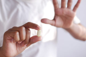 a person holds up a warning hand while offering a pill possibly about when to Quit oxycontin
