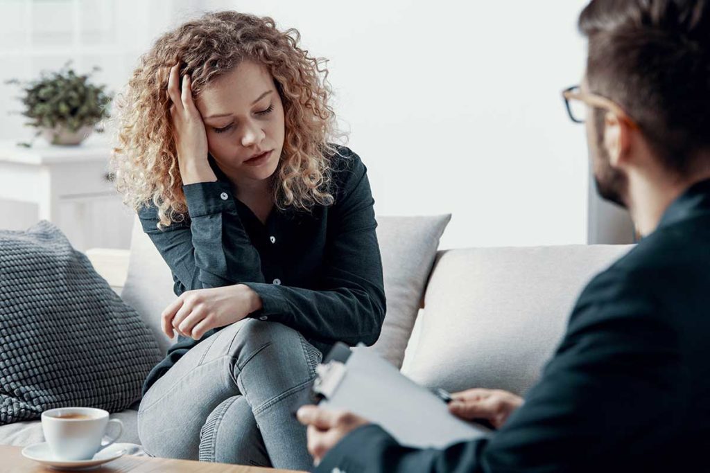 a person sits on a couch speaking to a therapist possibly struggling with Symptoms of meth use