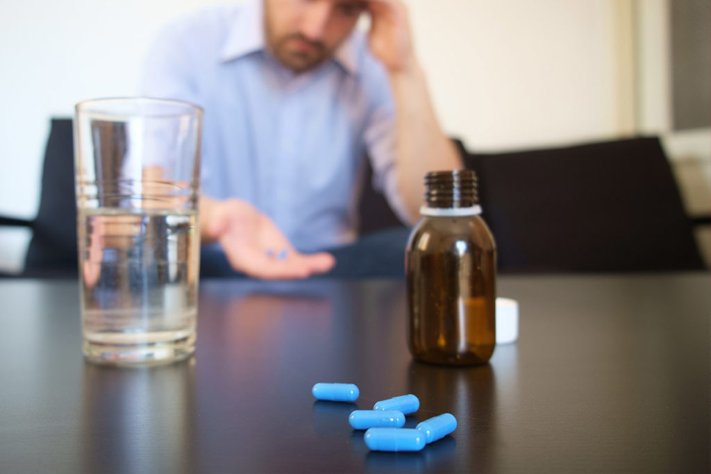 a person sits at a table with spilled pills on it possibly struggling with Symptoms of oxycontin use