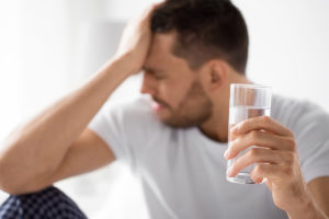 a person holds their head and a glass of water possibly wondering What are the stages of withdrawal