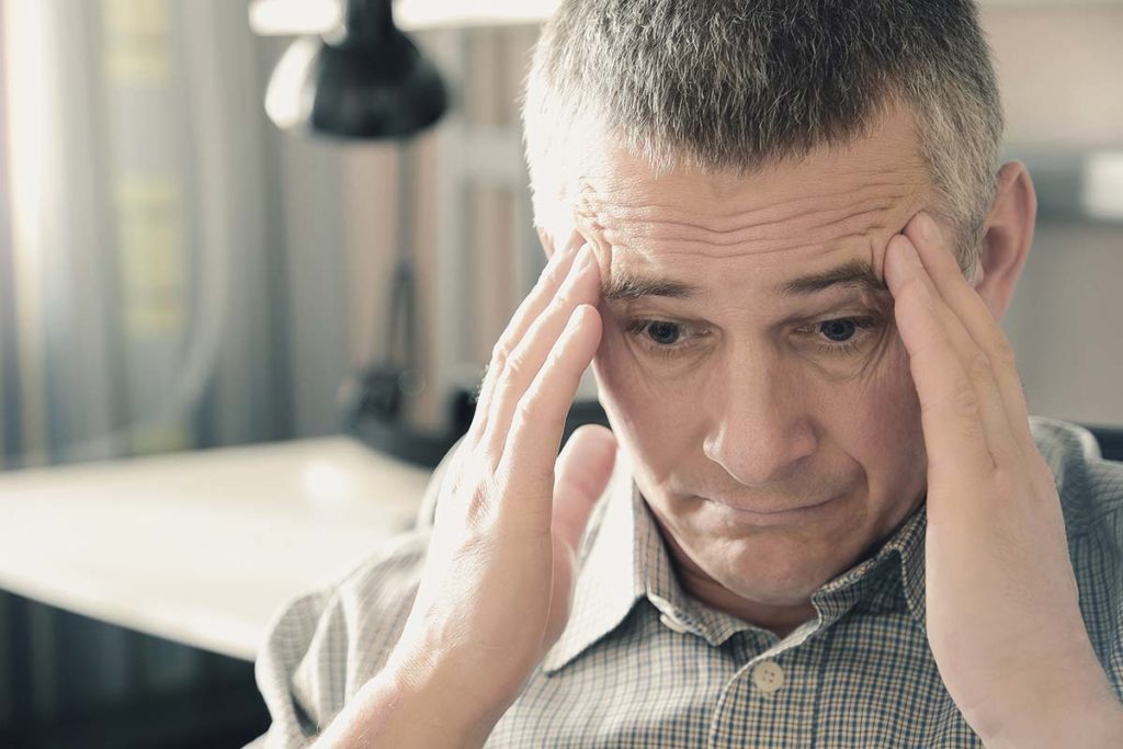 a person sits with their fingers on their temples experiencing wet brain symptoms