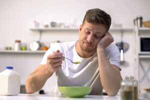 a person who doesn't look hungry while eating a bowl of food to show the link between alcohol and loss of appetite