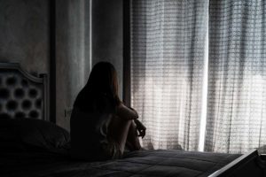 a person sits on a bed looking out a curtained window when learning about a heroin overdose