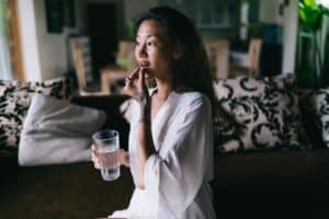 a woman takes her medicine with a glass of water while wondering of the effects of prescription drug abuse