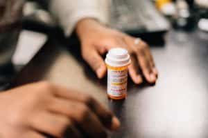 a set of hands on either side of a prescription bottle to represent prescription drug abuse