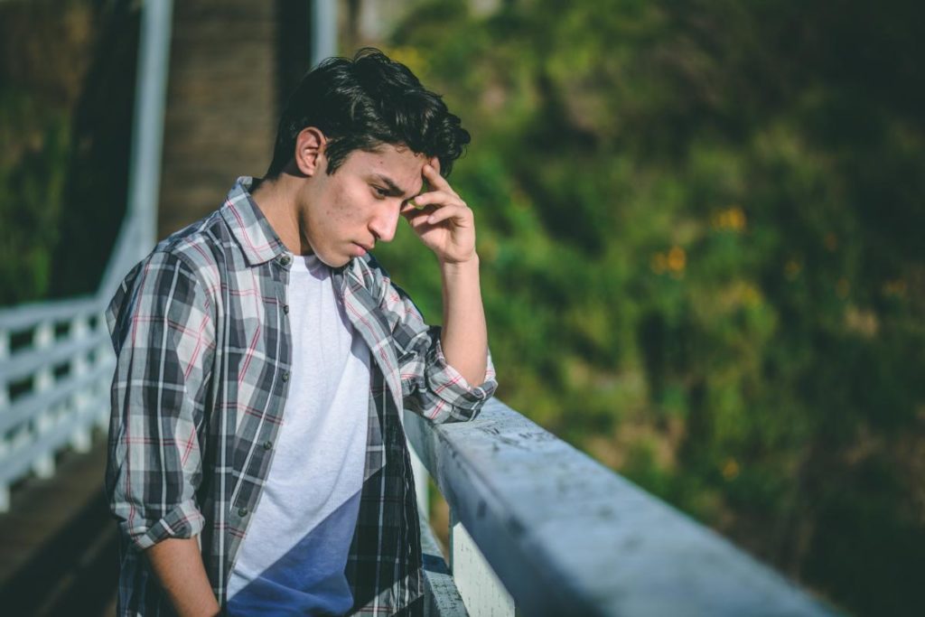 a person stairs over a railing sadly with their hand on their forehead as they learn of the long term effects of heroin