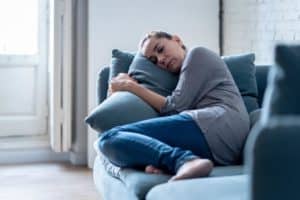 a person lays on a couch with their arms around a pillow as they are addicted to prescription drugs