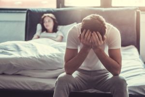 a couple looks angry while one sits on the edge of the bed and one folds their arms and sits up in bed experience how marijuana affects relationships