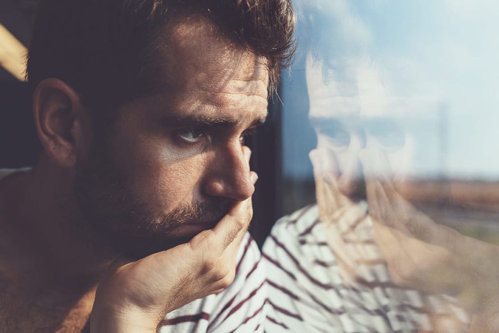 a person looks out of a window sadly wondering how to cope with suicidal thoughts