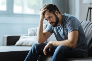 a person experiencing substance abuse puts their hand on their head while sitting on a bed and wonders about opiates vs opioids