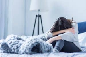 a person wraps their arms around their knees in bed while experiencing prescription drug addiction symptoms