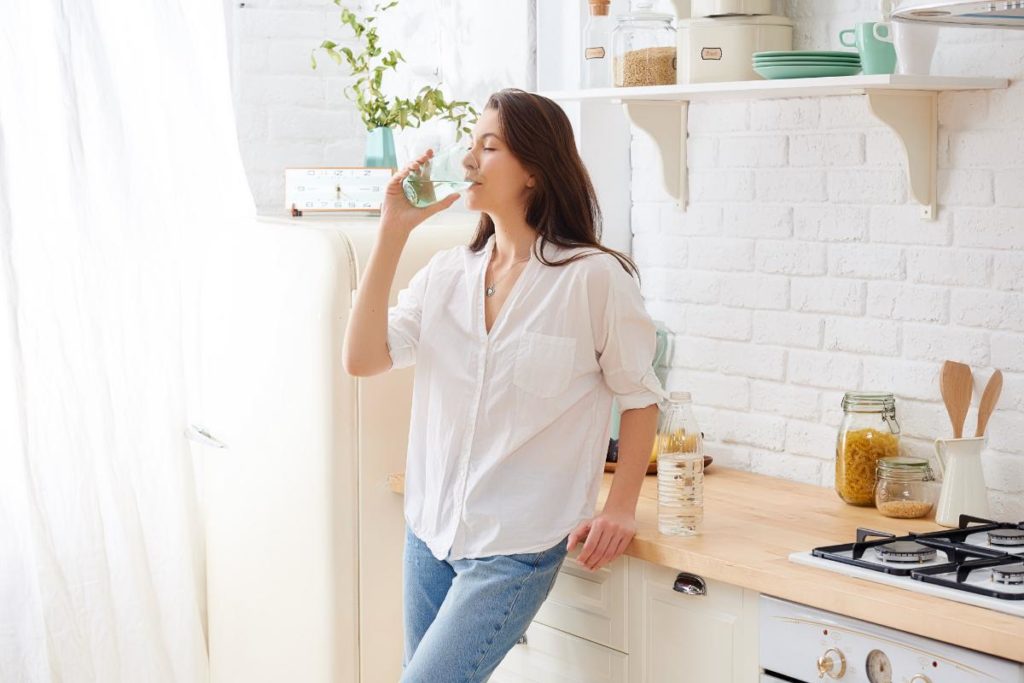 a person leans against the counter in their pristine kitchen while they drink water and live alcohol free