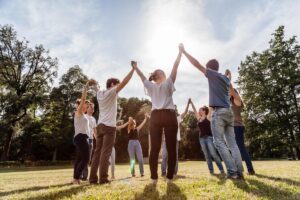 a group of people stands in a circle holding hands up to the sky outside to show a few group therapy activities for anxiety