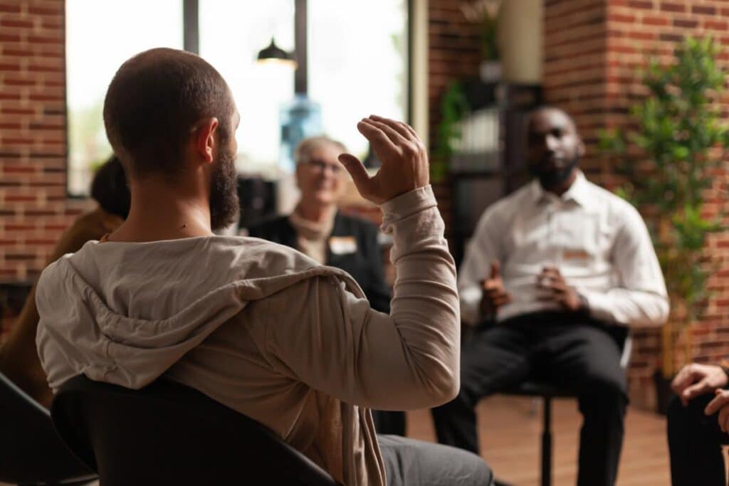 a person raises their hand in an alcohol rehab to talk about the hidden costs of alcoholism