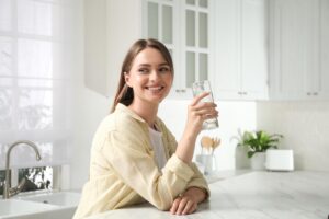 a person smiles and leans against a white counter in a white kitchen while drinking water to overcome drug addiction