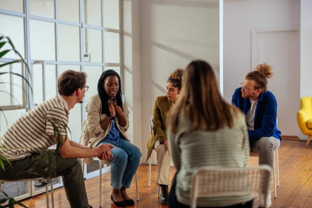 a group of people sit in chairs in a circle and talk during cocaine addiction treatment