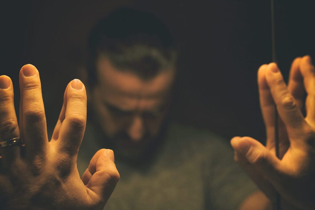 a person puts his fingers against a mirror while he looks down dramatically to show the dangers of oxycontin addiction