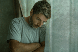 a person looks sad leaning against a window while experiencing the psychological effects of oxycontin