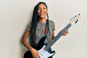 a young person with a guitar smiles at the camera to show the health benefits of music therapy