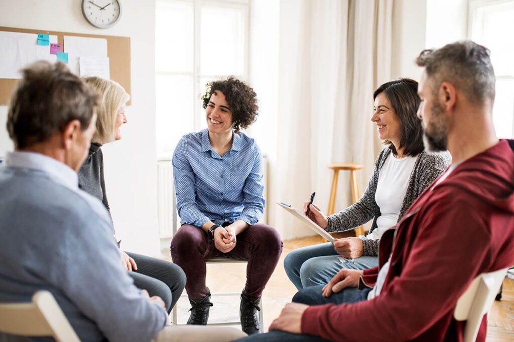 a group of people sit in chairs and participate in group therapy activities