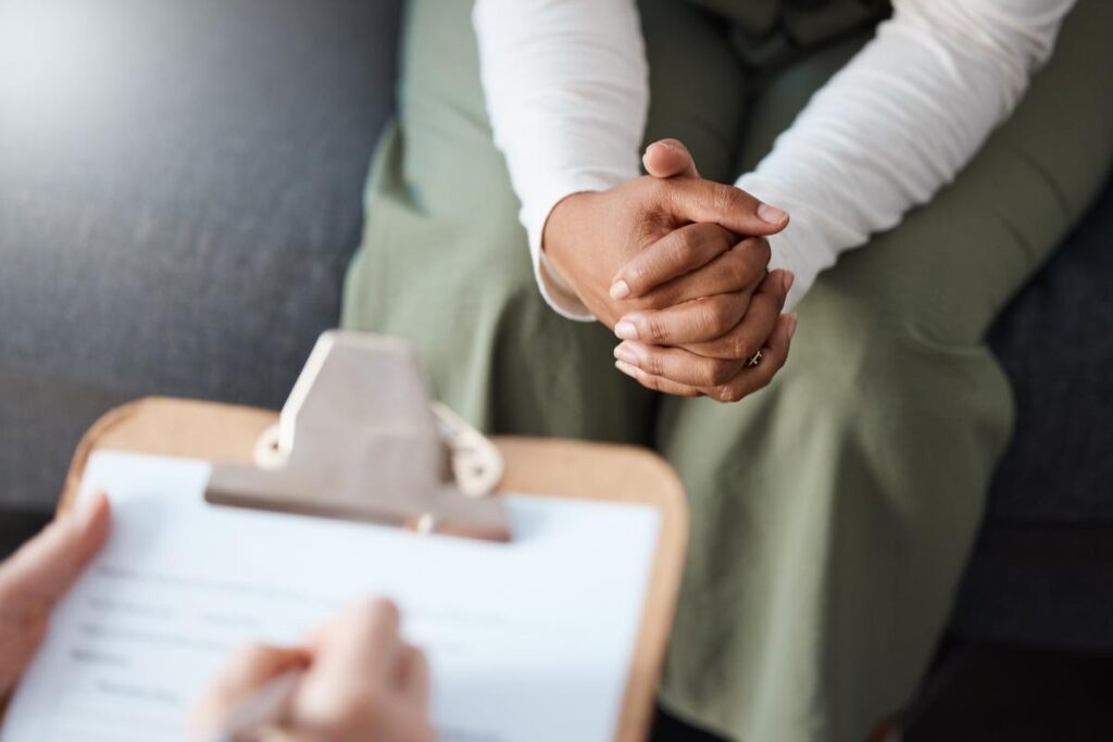 a patient folds their hands in front of someone with an intake form telling about the benefits of depression treatment programs