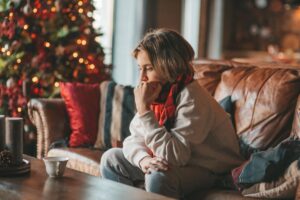 a person sits on a couch by a Christmas tree wondering how to cope with holiday stress and anxiety
